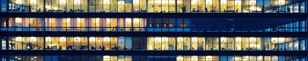 Exterior view of 3 floors of office windows lit up at night 